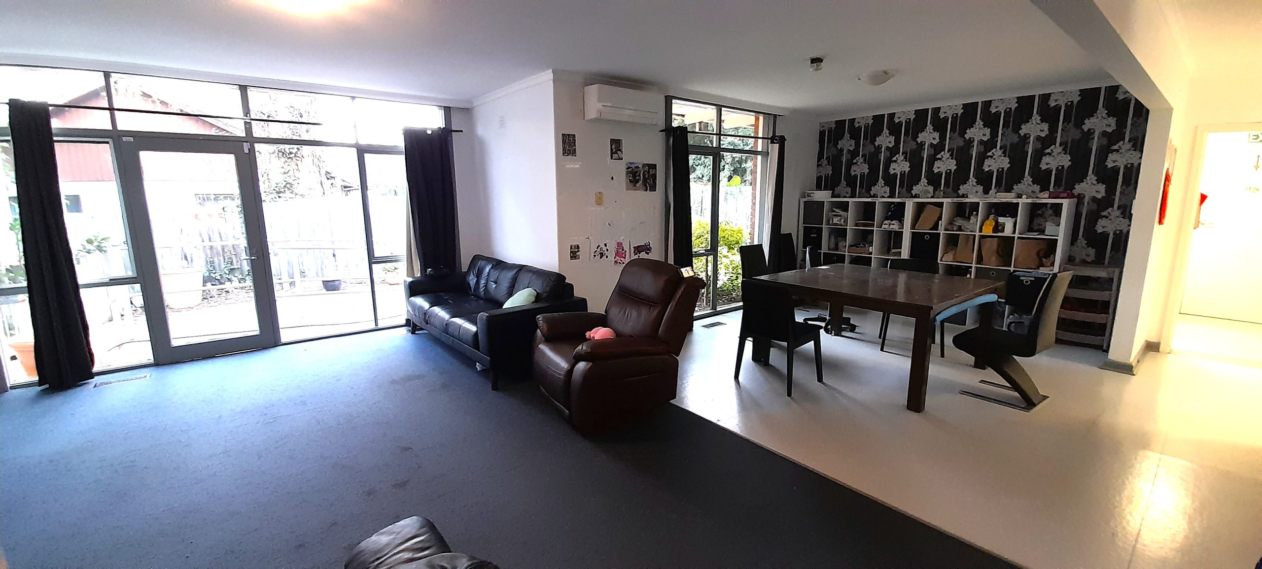 Lounge room with a couch and large window doors and an open plan dining room with a table and cubby shelves