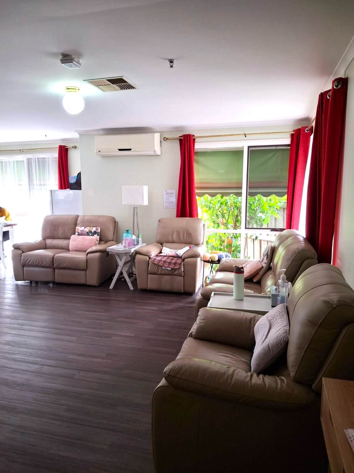 A lounge room with four couches/arm chairs and red curtains on large windows