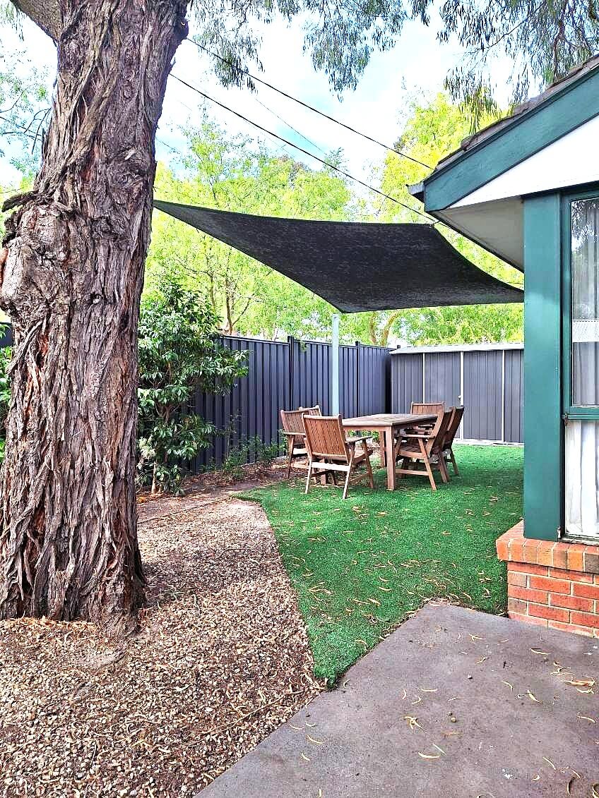 Small backyard with a large tree and a grassed area with an outdoor table and chairs