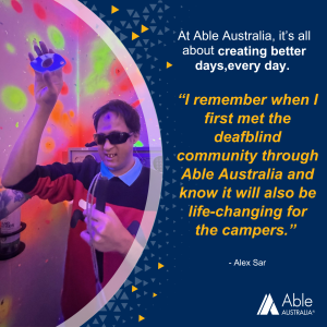 Person wearing sunglasses and a red and black jumper smiles while holding sensory objects in a room with colourful glowing paint. Text reads: ‘At Able Australia, it’s all about creating better days, every day. I remember when I first met the deafblind community through Able Australia and know it will also be life-changing for the campers.’ – Alex Sar.