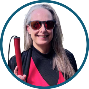 Kimberley is smiling and holding a red mobility cane. She is wearing a red vest with a black top underneath.