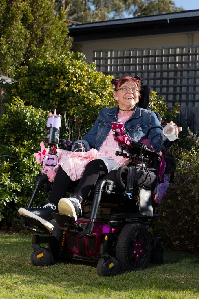 Margie in the garden siiting in her chair and smiling infectiously