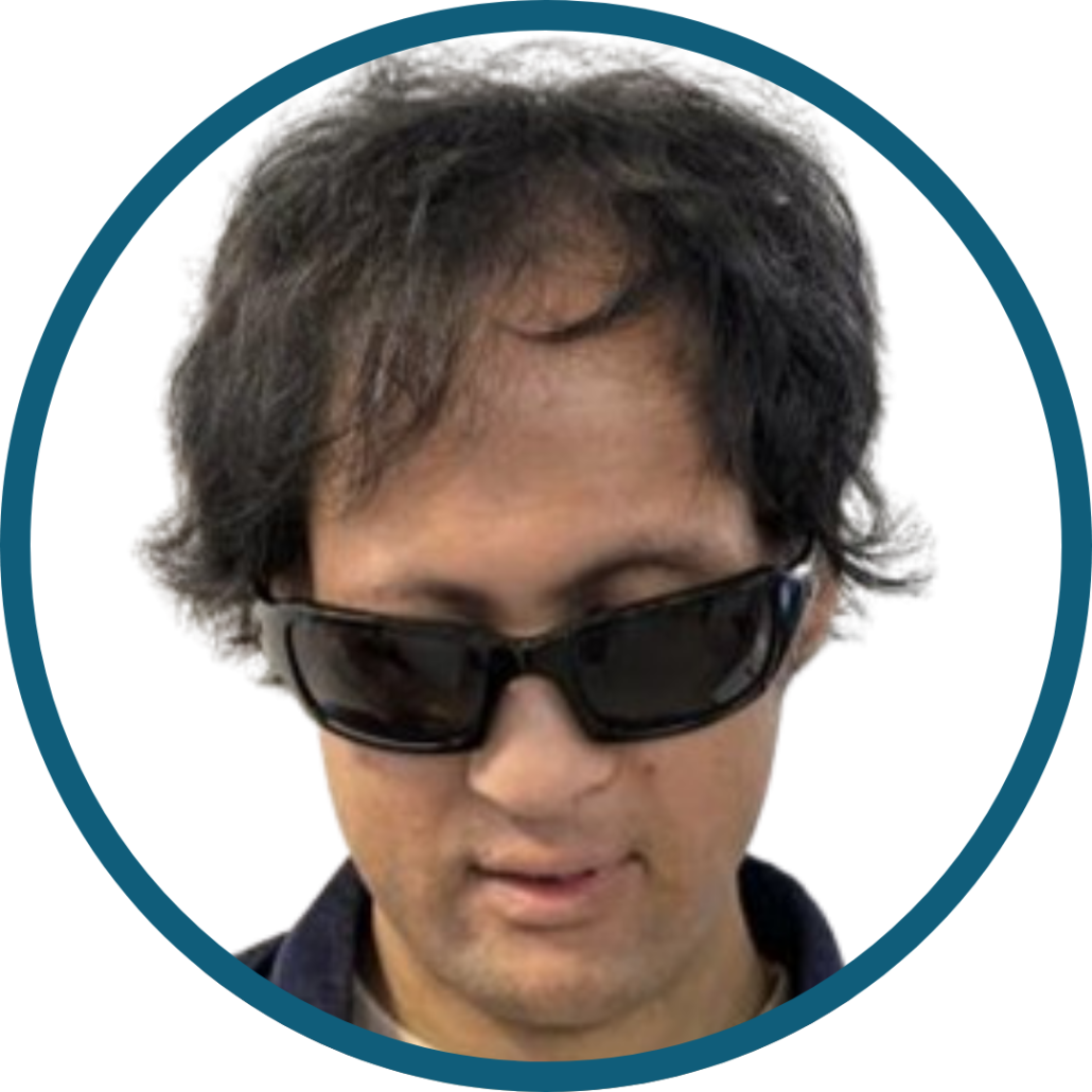 Alex is facing the camera directly. They are wearing dark sunglasses and have medium‑length, dark, slightly wavy hair. The background is plain white, and the image is framed by a teal circular border.