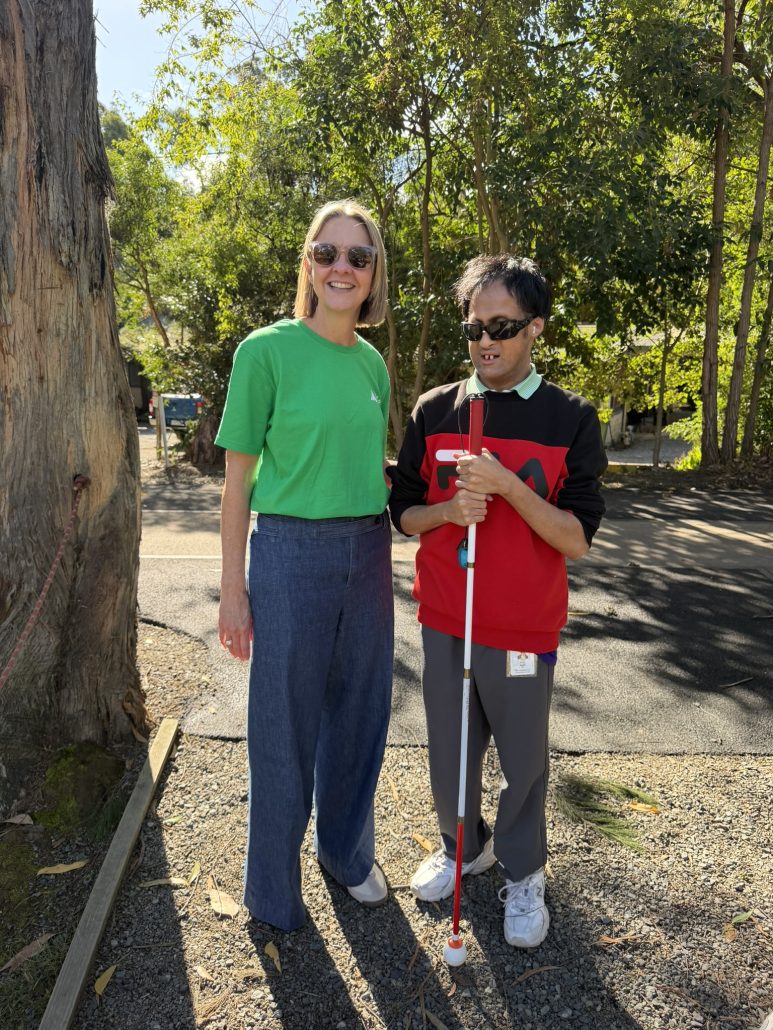Alex and Lynette McKeown CEO of Able Australia outsite at the Deafblind Camp 2026. They are both looking at the camera smiling with the sun shining behind them.