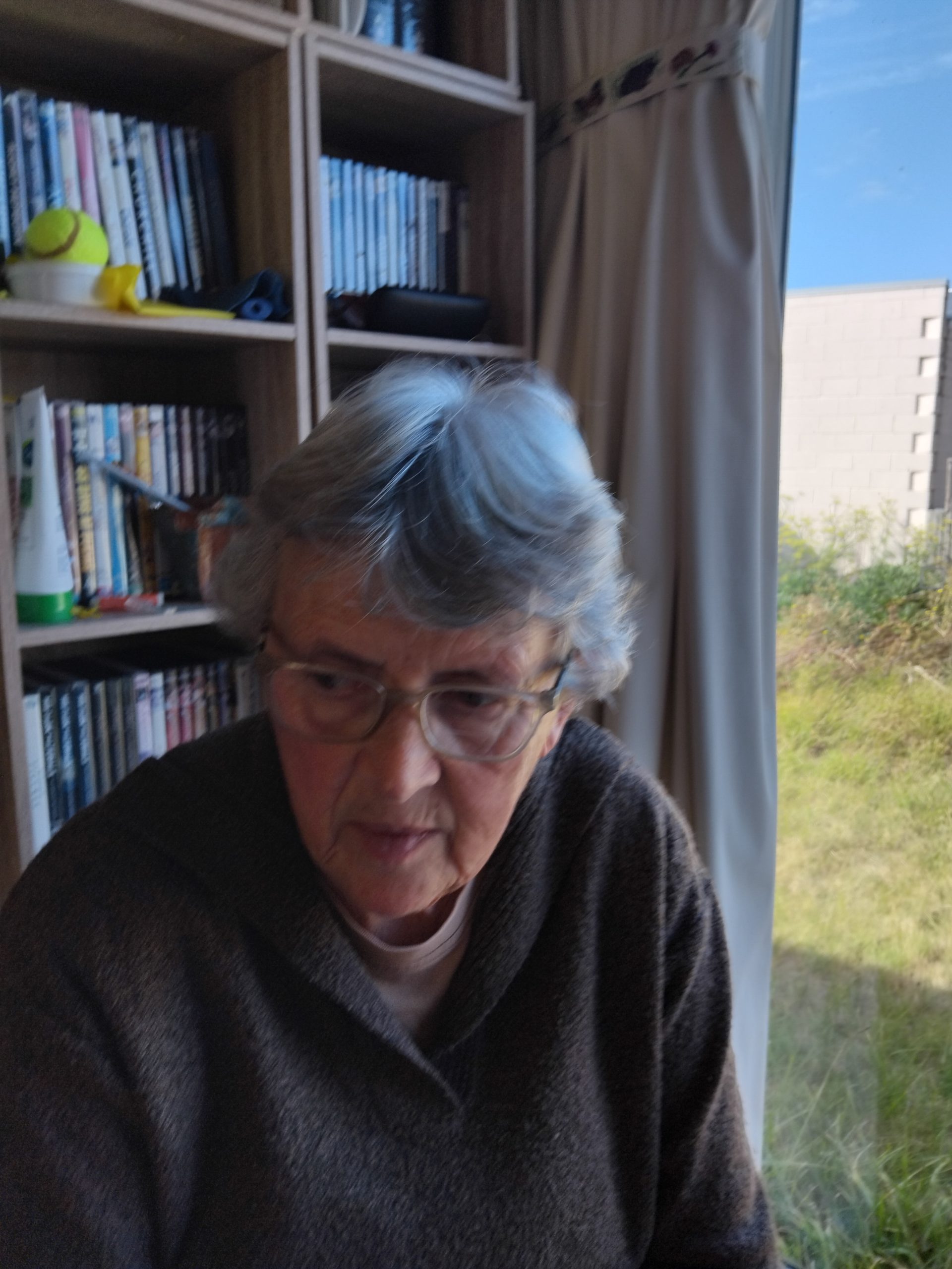 Laura sitting in a study. She is looking to the side wearing a jumper and glasses with short grey hair.